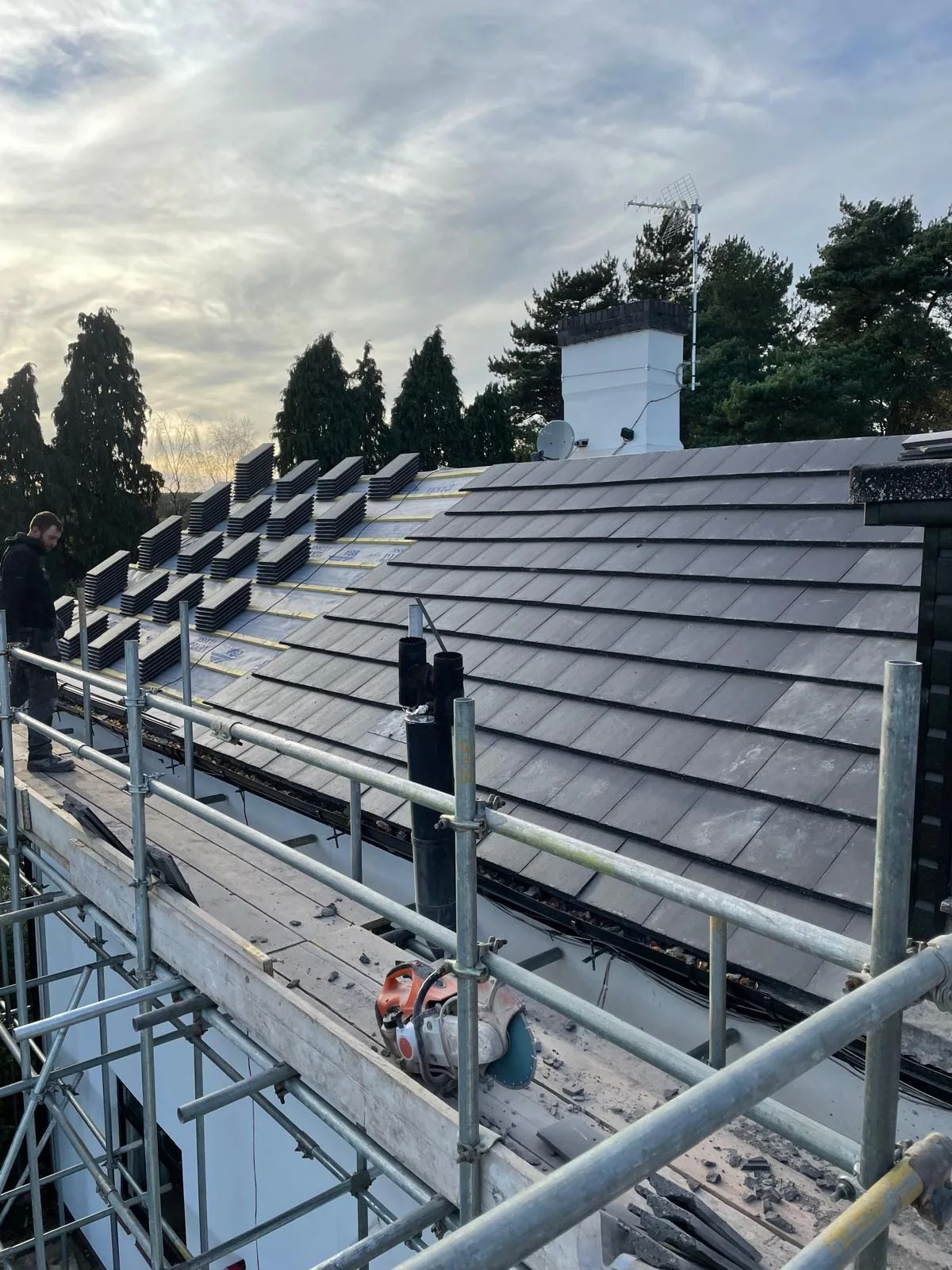 Roofer on scaffolding laying new dark grey roof tiles